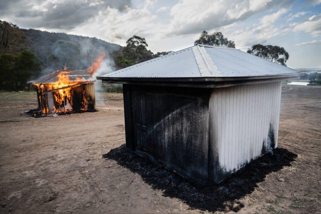 A shed painted with FSA Firecoat undercoat is less damaged by fire than the burning building in the background.